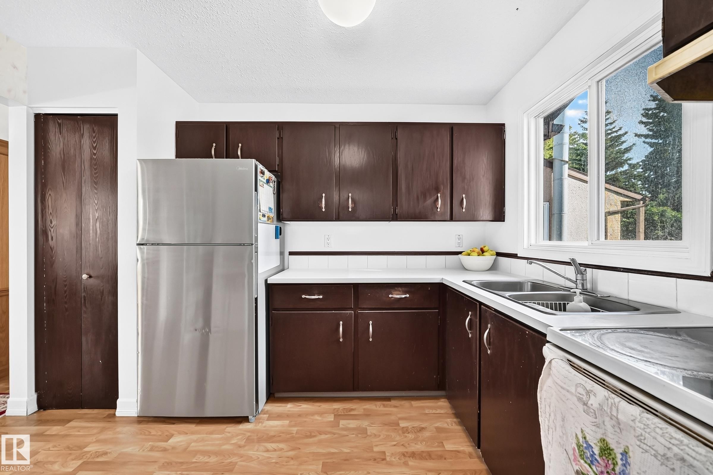 Kitchen featuring wood-finish flooring, dark wood cabinetry, a double basin stainless steel sink, and a white tiled backsplash - 11007 173A Avenue Nw, Edmonton, AB