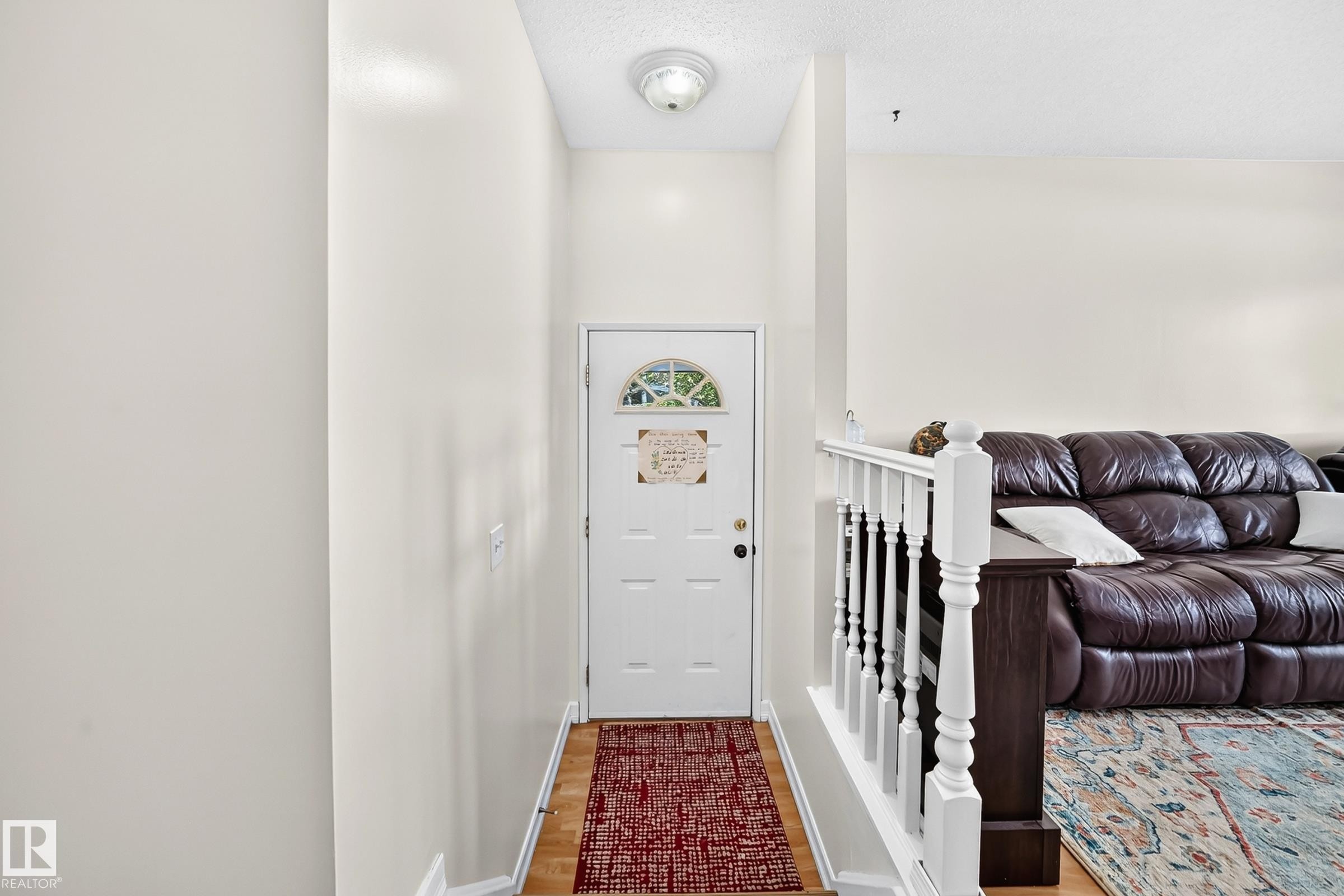 Recessed entry with wood-finish flooring, white paneled door with an arched glass insert, and a ceiling-mounted light fixture - 11007 173A Avenue Nw, Edmonton, AB