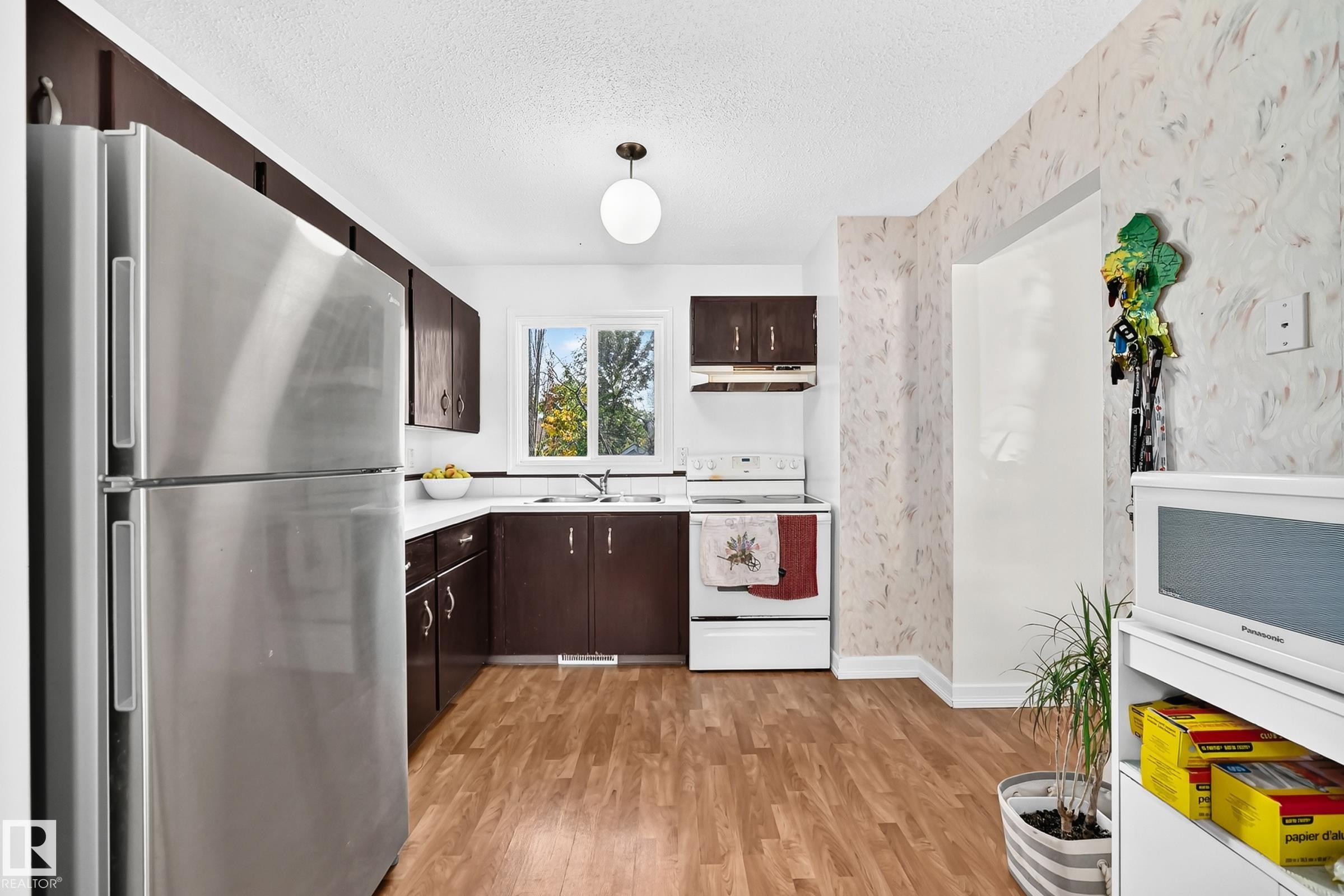 Kitchen featuring wood-finish flooring, dark wood-finish cabinetry, white countertops, and white appliances - 11007 173A Avenue Nw, Edmonton, AB