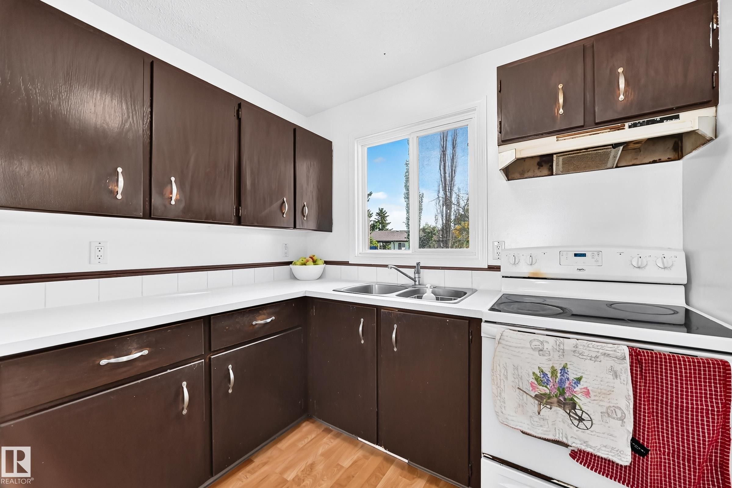 Kitchen featuring dark-finish cabinetry, white countertops, a double basin sink, white tile backsplash, and wood-finish flooring - 11007 173A Avenue Nw, Edmonton, AB