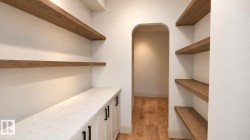 Built-in cabinetry with dark hardware, a light-toned countertop, and wood-finish open shelving - 
