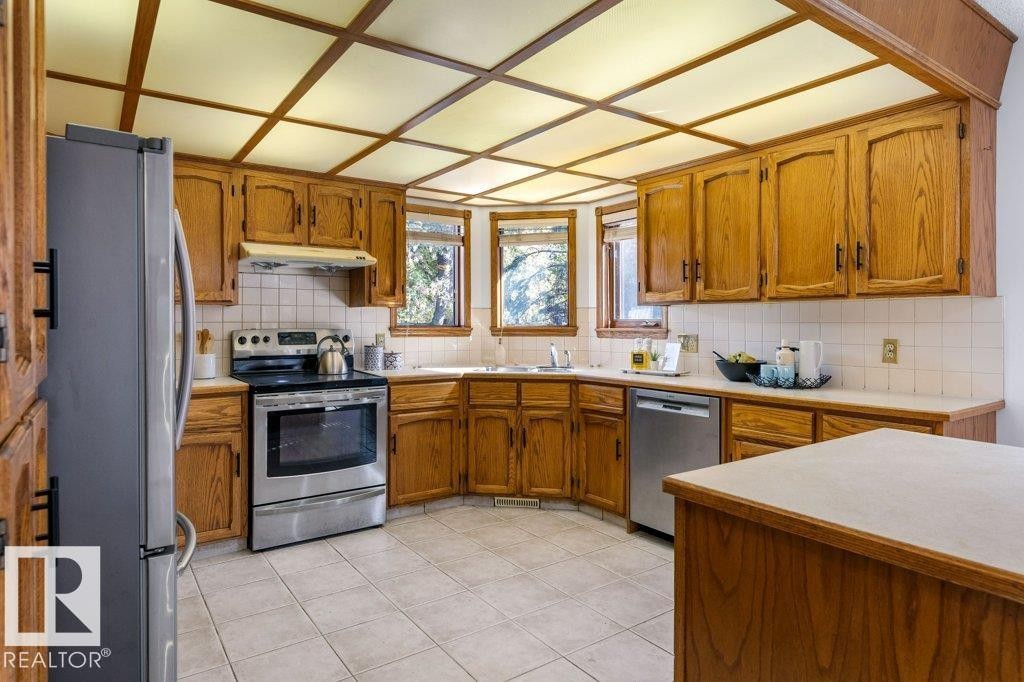 Kitchen featuring wood cabinetry, stainless steel appliances, a tile backsplash, and a coffered ceiling with inset lighting - 507 Burton Close Nw, Edmonton, AB