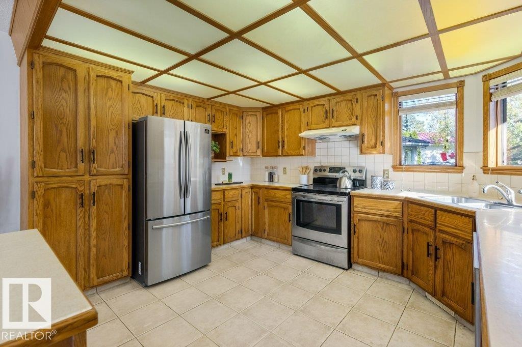 Kitchen featuring wood cabinetry, stainless steel appliances, tile flooring, and a coffered ceiling - 507 Burton Close Nw, Edmonton, AB