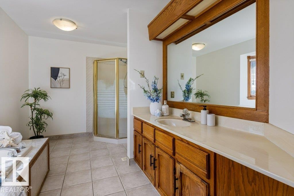 Wood-finish vanity with integrated sink, expansive mirror, and corner shower enclosure, complemented by tiled flooring and an integrated soaking tub - 507 Burton Close Nw, Edmonton, AB