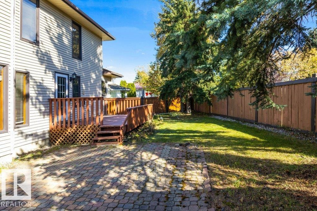 Exterior featuring a multi-level wood deck with railing, a paved patio area, a fenced yard, and mature trees - 507 Burton Close Nw, Edmonton, AB