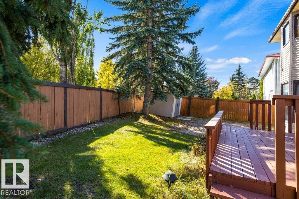 Backyard featuring a wooden privacy fence, mature evergreen trees, a green lawn, and a wood-finish deck - 507 Burton Close Nw, Edmonton, AB