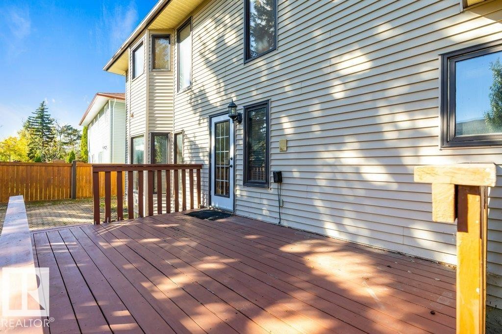 Expansive rear deck with wood railing, leading to a brick paver patio and full privacy fencing - 507 Burton Close Nw, Edmonton, AB
