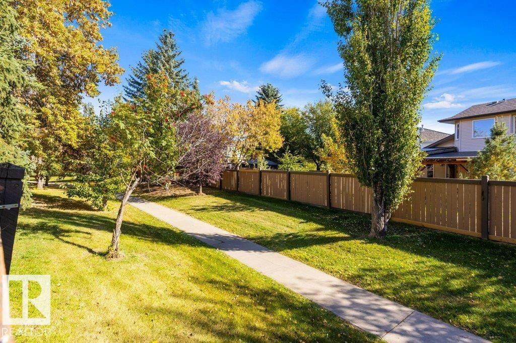 Expansive outdoor space featuring a paved pathway, mature trees, and a wooden privacy fence - 507 Burton Close Nw, Edmonton, AB