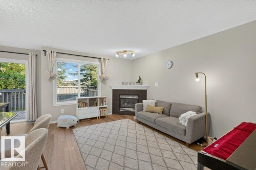 Wood-finish flooring, corner fireplace with tile surround, large window, and direct access to an outdoor deck - #41 287 Macewan Rd Sw, Edmonton, AB 