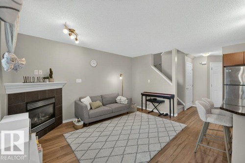 Wood-finish flooring, tiled fireplace with mantel, staircase with white railing, built-in cabinetry, and stainless steel appliances - #41 287 Macewan Rd Sw, Edmonton, AB 