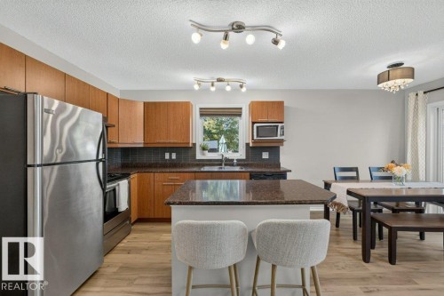 Kitchen featuring wood-finish cabinetry, stainless steel refrigerator, dark countertops, and wood-finish flooring - #41 287 Macewan Rd Sw, Edmonton, AB 