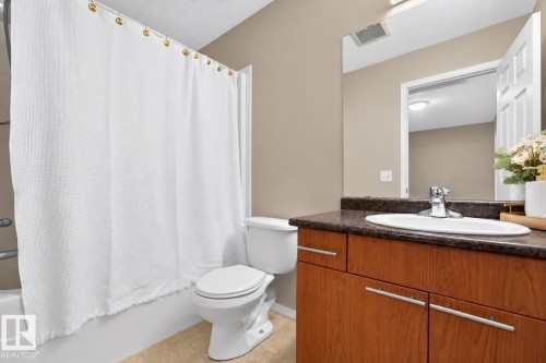 Bathroom featuring a single vanity with wood-finish cabinetry, a dark countertop, and a white drop-in sink with a chrome faucet - #41 287 Macewan Rd Sw, Edmonton, AB 