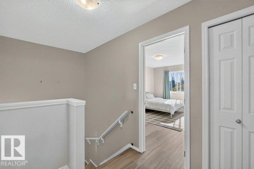 Hallway featuring neutral wall paint, wood-finish flooring, white trim, and a flush-mount ceiling light - #41 287 Macewan Rd Sw, Edmonton, AB 