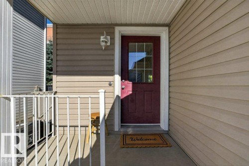 Front entry with red panel door and decorative glass insert, complemented by a white metal railing and light-colored siding - #41 287 Macewan Rd Sw, Edmonton, AB 