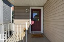 Front entry with red panel door and decorative glass insert, complemented by a white metal railing and light-colored siding - #41 287 Macewan Rd Sw, Edmonton, AB 