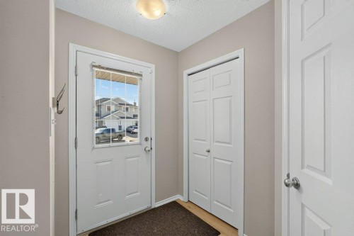Entryway featuring a white paneled door with glass insert, light-toned wood-finish flooring, and a built-in bi-fold closet - #41 287 Macewan Rd Sw, Edmonton, AB 