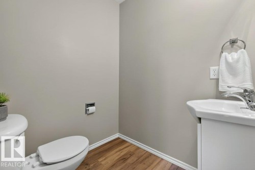 Light gray walls with white trim, wood-finish flooring, white toilet, and white pedestal sink - #41 287 Macewan Rd Sw, Edmonton, AB 