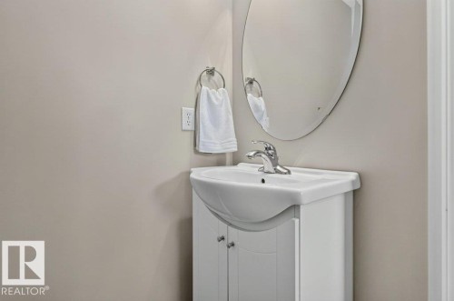 White vanity with cabinet storage, integrated sink, chrome faucet, and an oval wall mirror - #41 287 Macewan Rd Sw, Edmonton, AB 