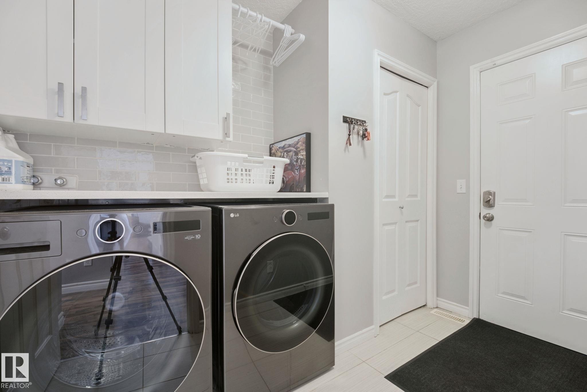 Laundry area featuring white cabinetry, a light-toned countertop, and a tiled backsplash - 324 Ascott Crescent, Sherwood Park, AB