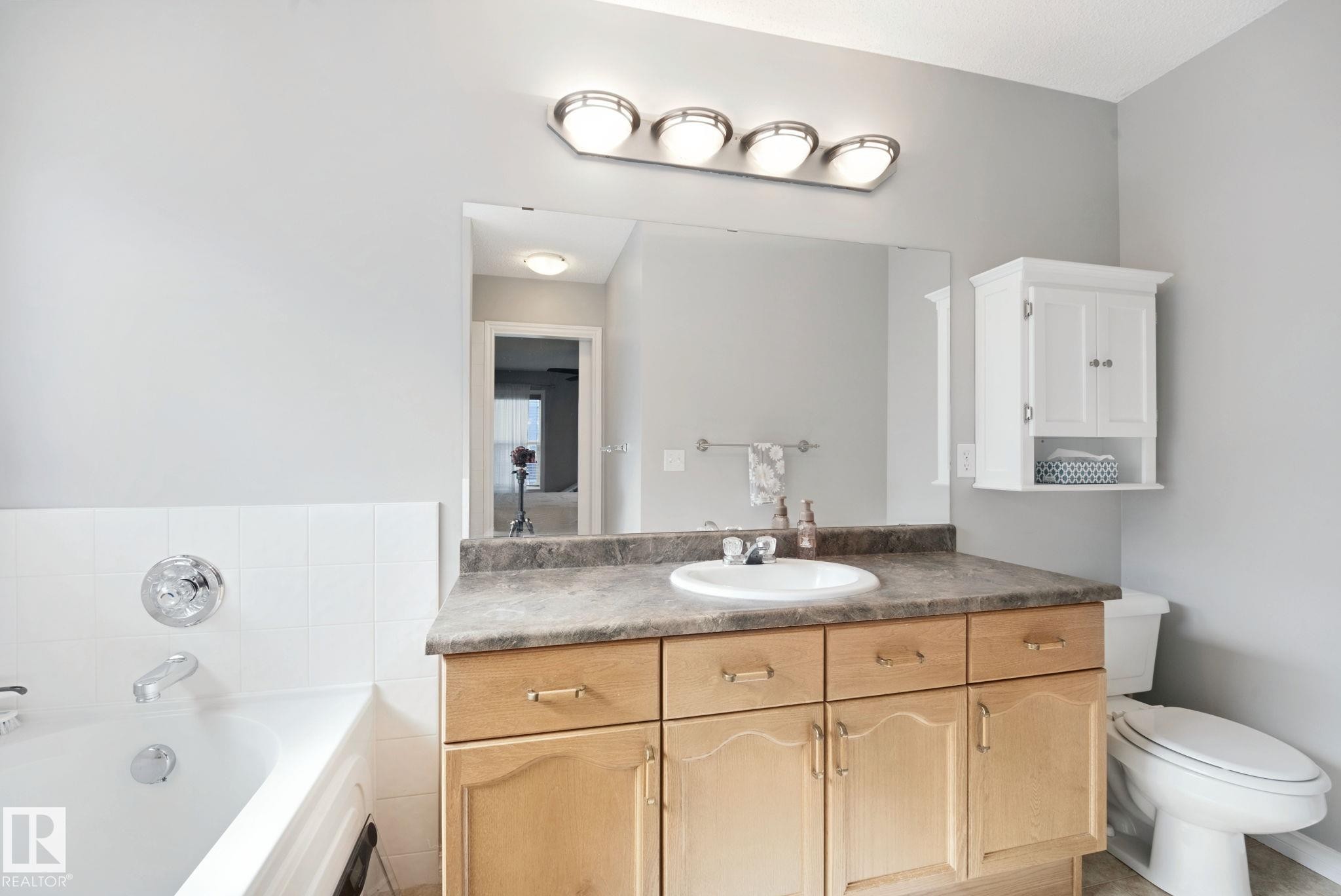 Full vanity with an integrated sink, surface-mount lighting, wall-mounted storage cabinet, and a built-in tub with tile surround - 324 Ascott Crescent, Sherwood Park, AB