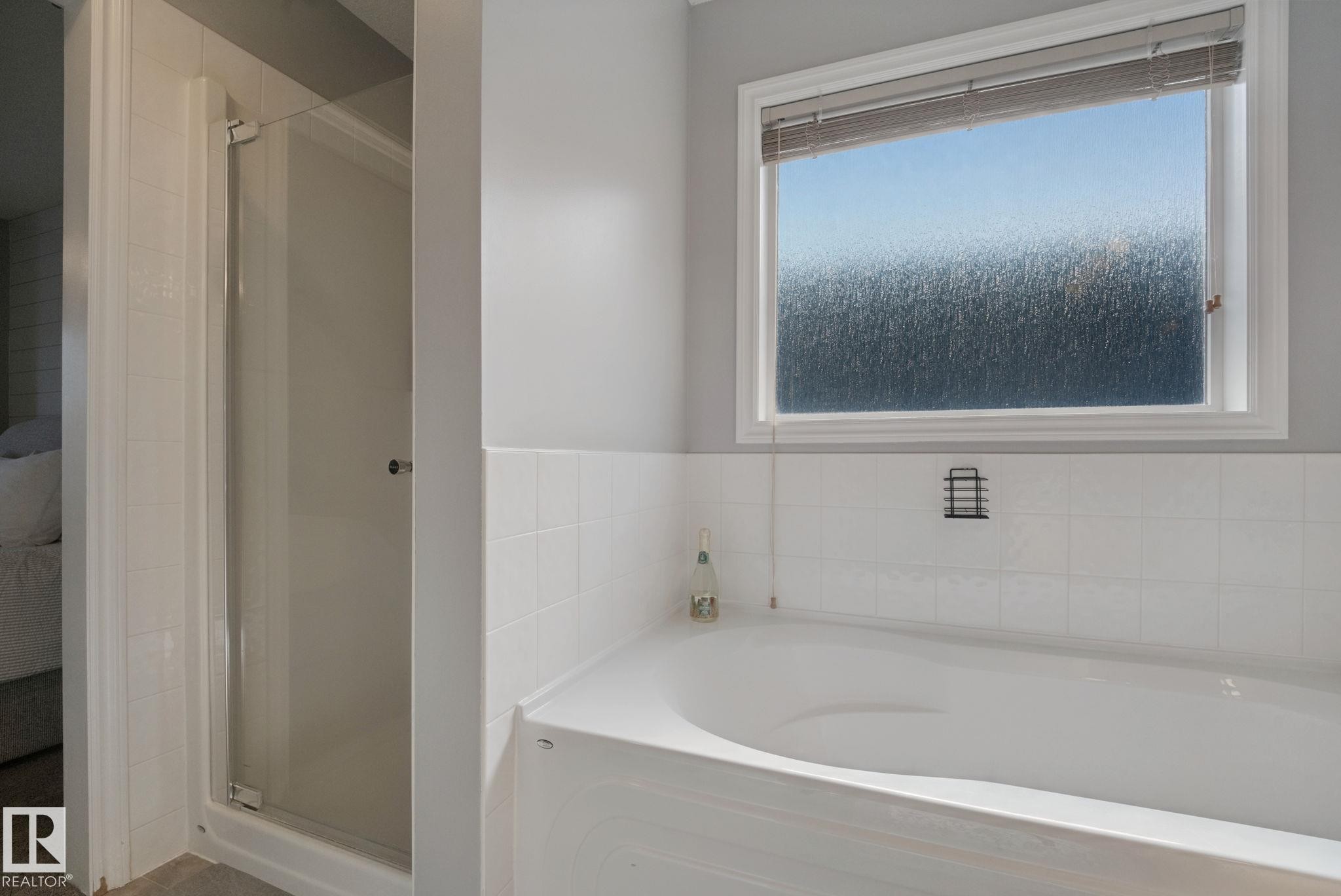 Built-in bathtub with white tile surround, privacy glass window, and an enclosed shower - 324 Ascott Crescent, Sherwood Park, AB