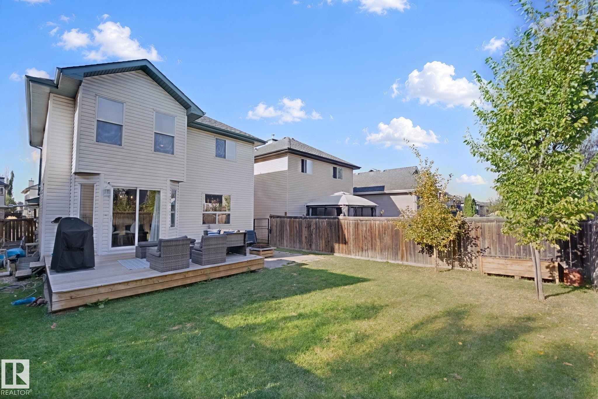 Spacious backyard featuring a wood deck, sliding glass door access, privacy fencing, and mature trees - 324 Ascott Crescent, Sherwood Park, AB