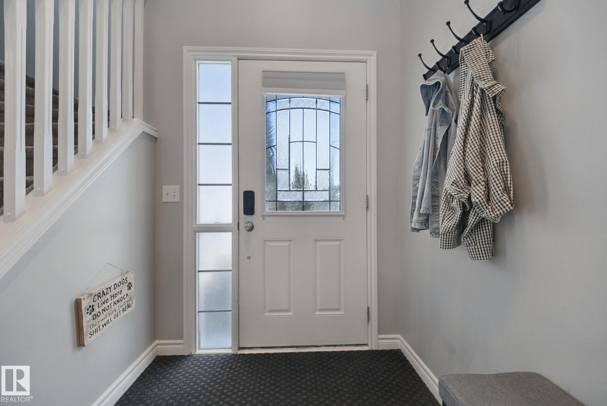 Entryway featuring a solid wood door with leaded glass, an adjacent sidelight with privacy glass, dark textured flooring, and a white staircase with balusters - 324 Ascott Crescent, Sherwood Park, AB