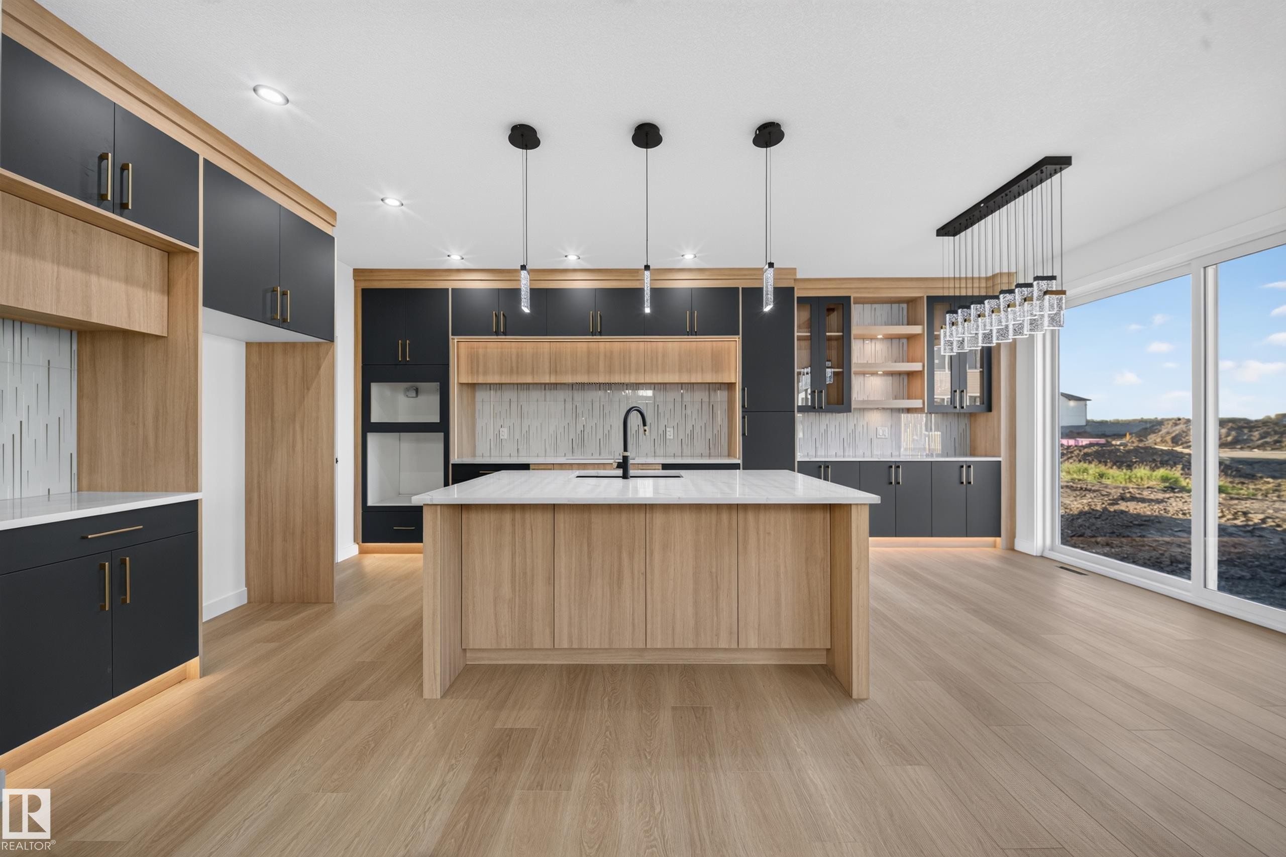 Contemporary kitchen featuring an expansive center island with countertop, two-tone cabinetry, wood-finish flooring, a full-height tile backsplash, and built-in appliances - 13024 186 Avene Nw, Edmonton, AB