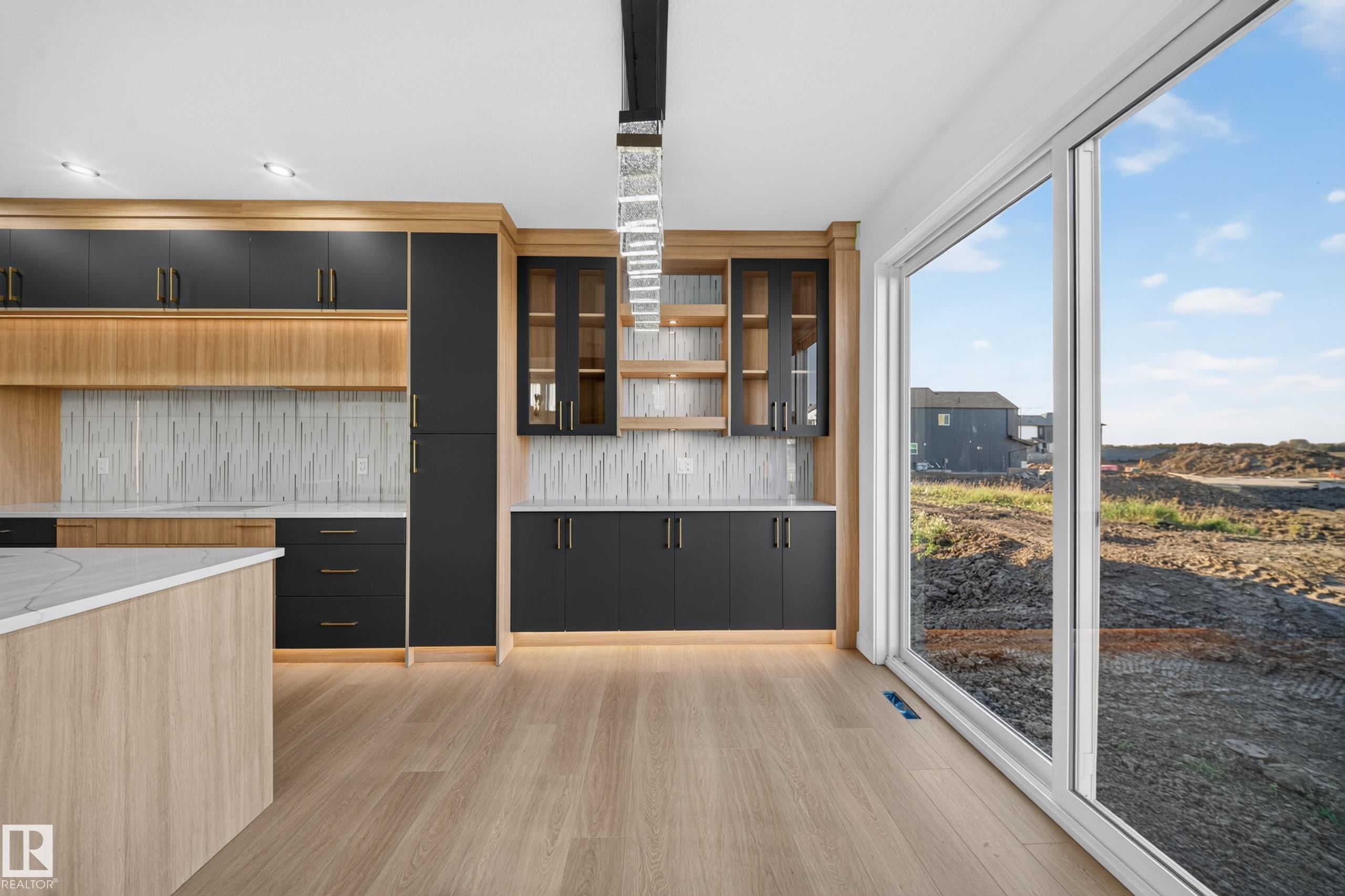 Kitchen featuring two-tone cabinetry with integrated lighting, a white textured backsplash, and a large central island with a light-toned countertop - 13024 186 Avene Nw, Edmonton, AB