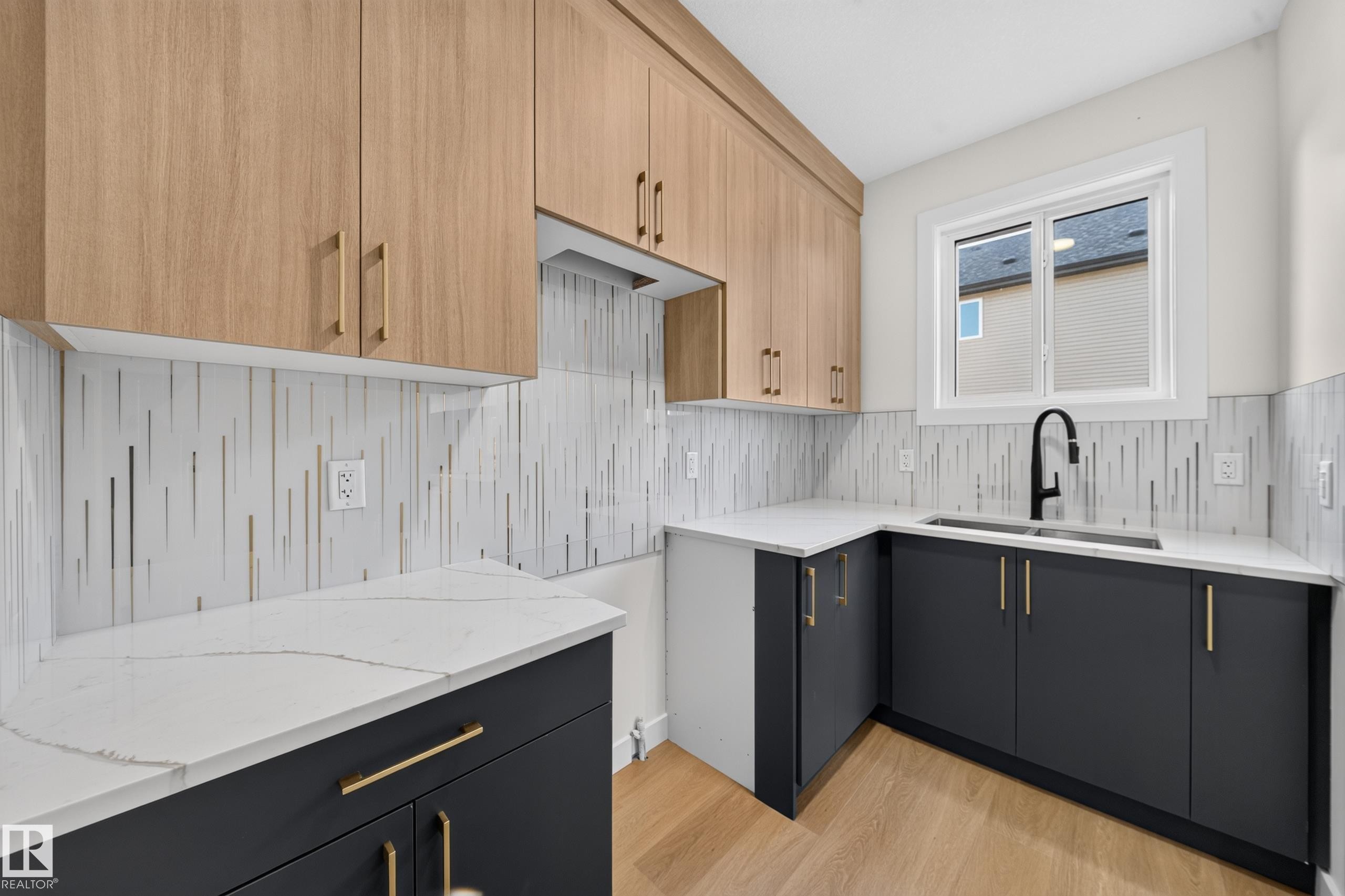 Two-tone cabinetry with wood-finish upper cabinets and dark lower cabinets, white countertops, modern backsplash, and a black gooseneck faucet - 13024 186 Avene Nw, Edmonton, AB