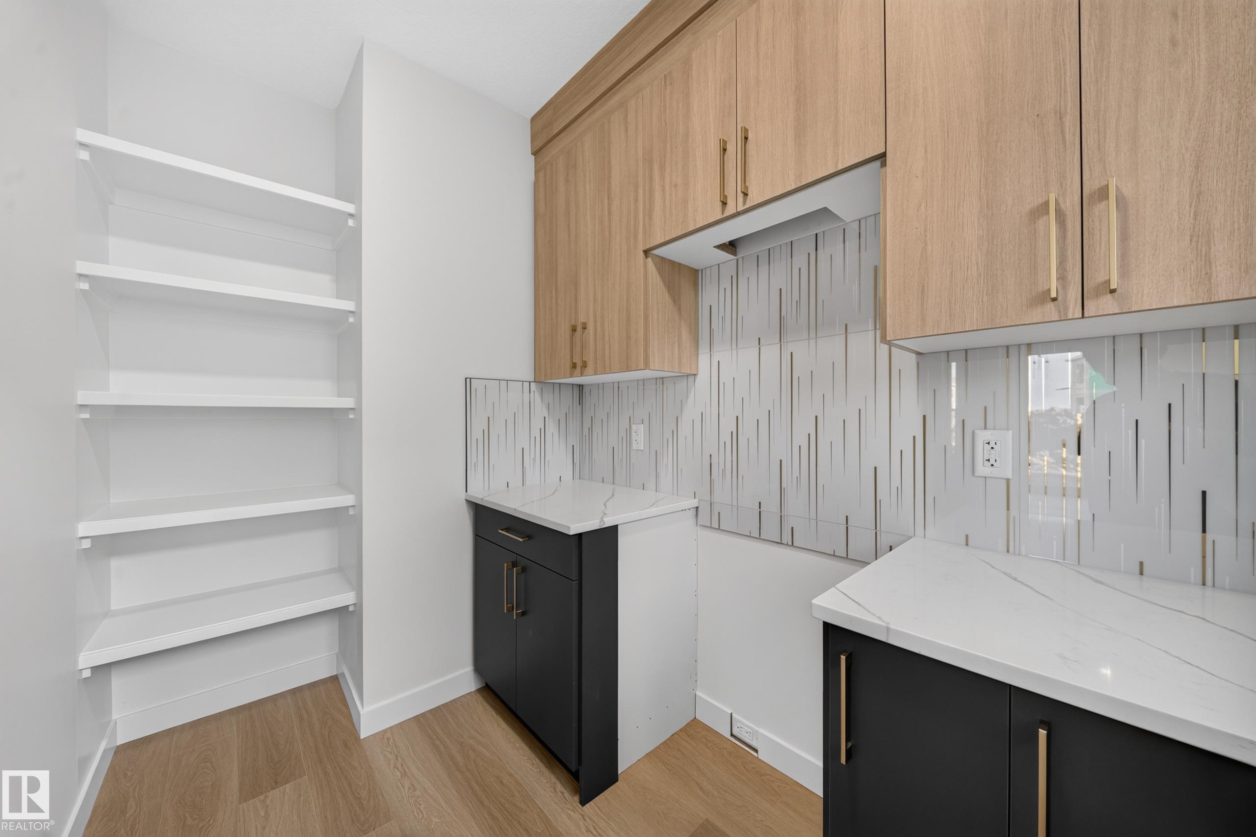 Built-in shelving, wood-finish flooring, light wood-tone upper cabinetry, dark lower cabinetry, and a patterned backsplash - 13024 186 Avene Nw, Edmonton, AB