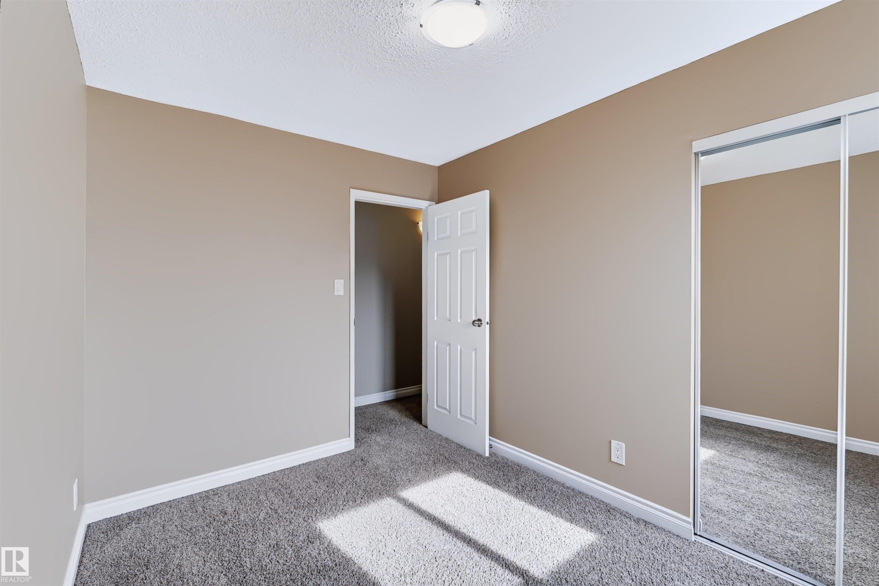 Neutral-toned walls, textured carpet flooring, white trim, interior door, and mirrored closet doors - 155 Primrose Gardens Gardens Nw, Edmonton, AB