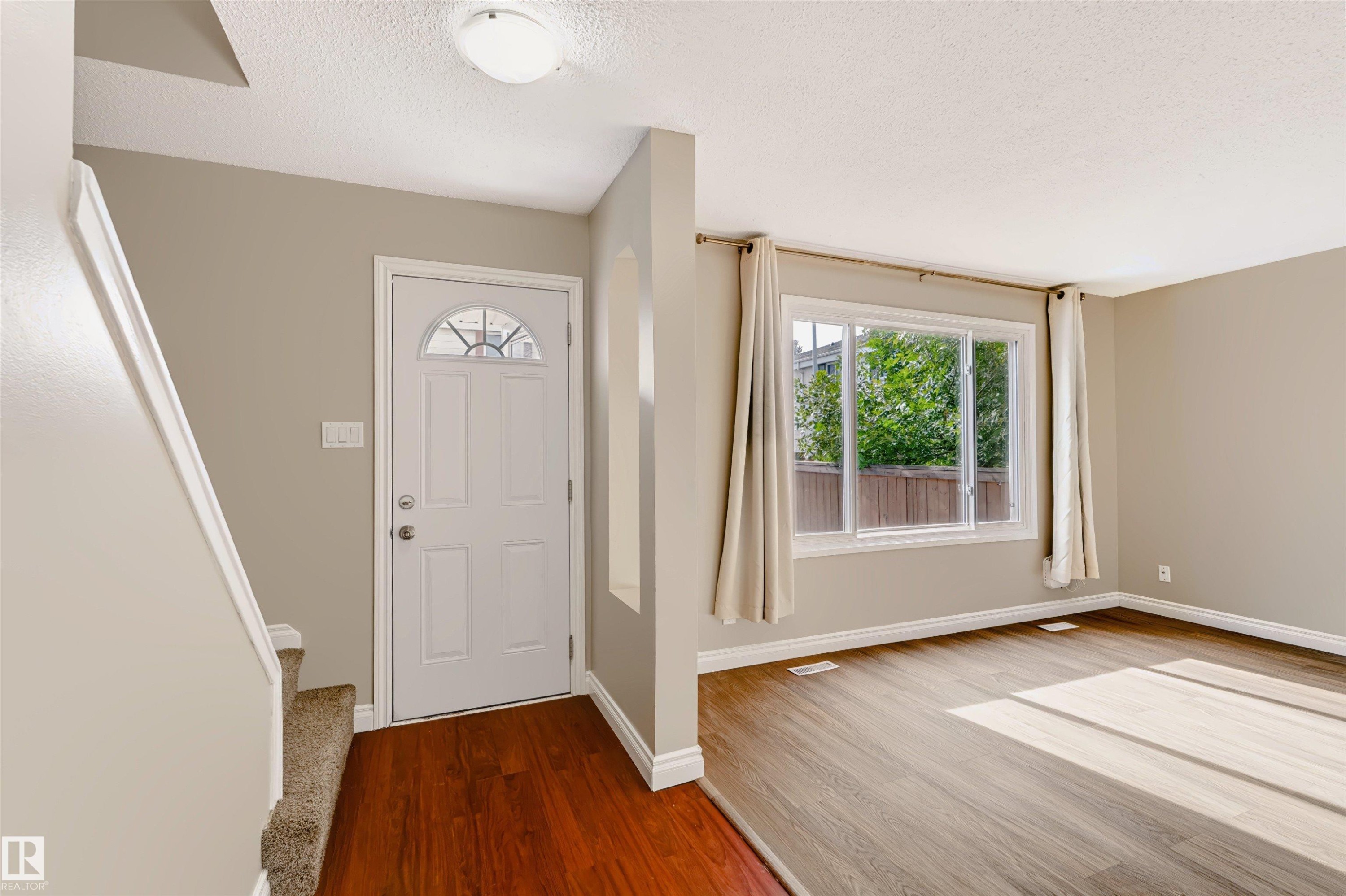 Entryway featuring a white paneled door with decorative glass, wood-finish flooring, and a flush mount ceiling light - 155 Primrose Gardens Gardens Nw, Edmonton, AB