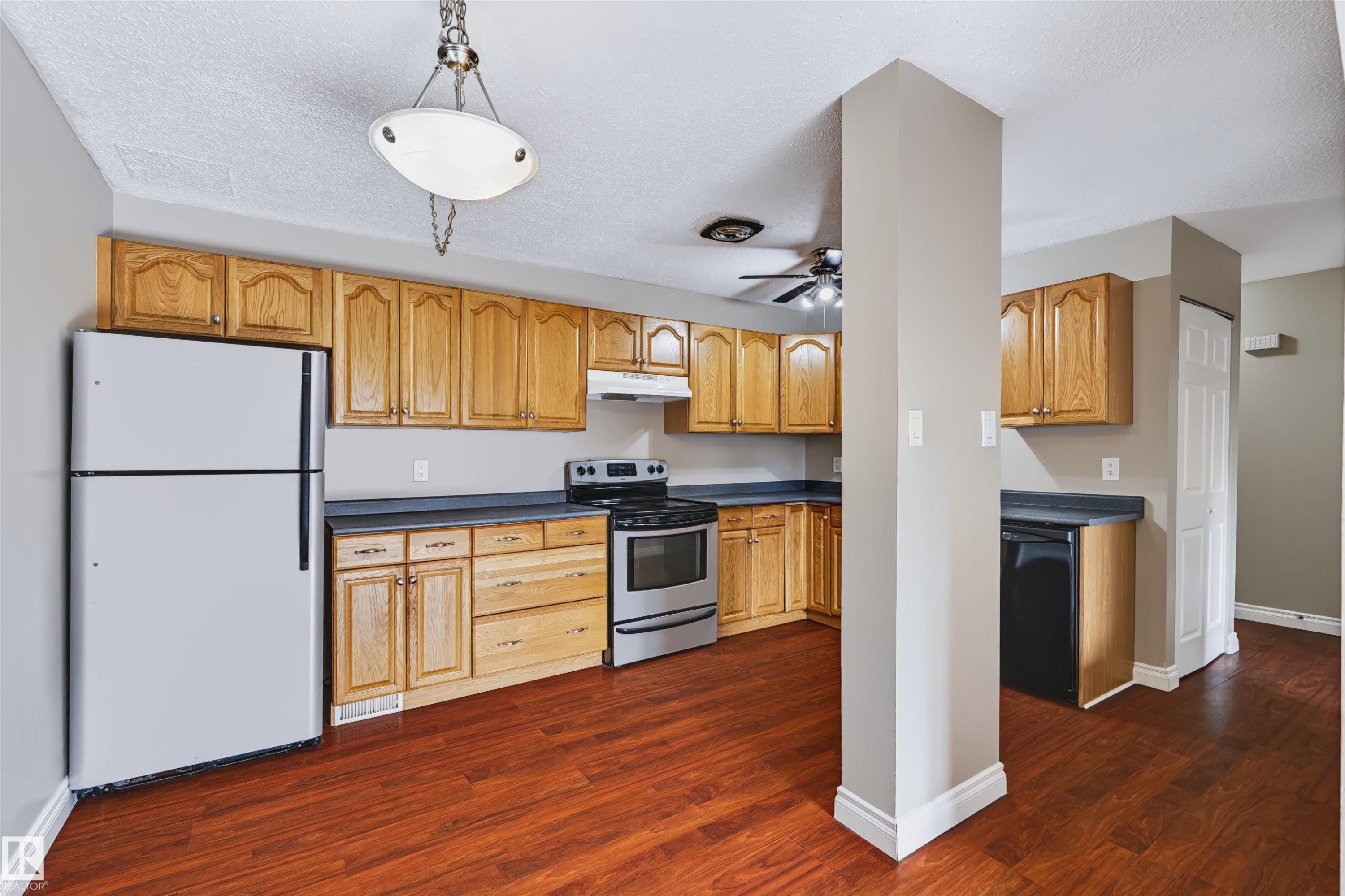 Kitchen featuring wood-finish cabinetry, dark countertops, and stainless steel appliances - 155 Primrose Gardens Gardens Nw, Edmonton, AB