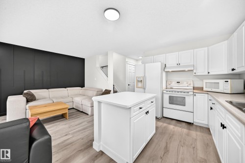 Open-concept living space with wood-finish flooring, a kitchen island, and white cabinetry - #27 287 Macewan Rd Sw, Edmonton, AB 