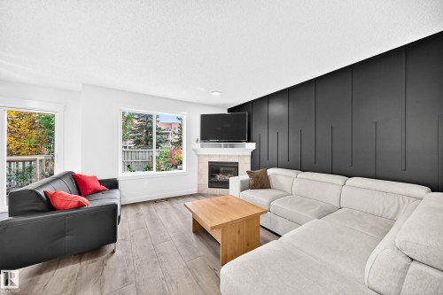 Corner fireplace with tile surround, wood-finish flooring, accent wall with vertical paneling, and multiple windows - #27 287 Macewan Rd Sw, Edmonton, AB 