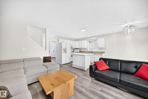 Open-concept living area featuring wood-finish flooring, white cabinetry, a kitchen island, and a built-in dishwasher - #27 287 Macewan Rd Sw, Edmonton, AB 