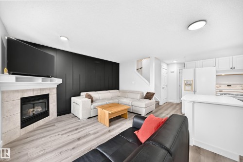 Living area with wood-finish flooring, a tile-surround fireplace, and a textured accent wall - #27 287 Macewan Rd Sw, Edmonton, AB 