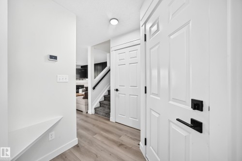 Wood-finish flooring, white paneled doors with matte black hardware, built-in shelving, and a carpeted staircase with a black handrail - #27 287 Macewan Rd Sw, Edmonton, AB 
