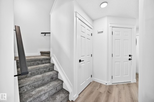 Carpeted staircase with black modern handrails, light wood-finish flooring, and white paneled doors with black hardware - #27 287 Macewan Rd Sw, Edmonton, AB 