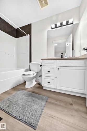 White vanity with shaker-style cabinetry, wood-finish flooring, and a white bathtub with dark-tiled surround - #27 287 Macewan Rd Sw, Edmonton, AB 