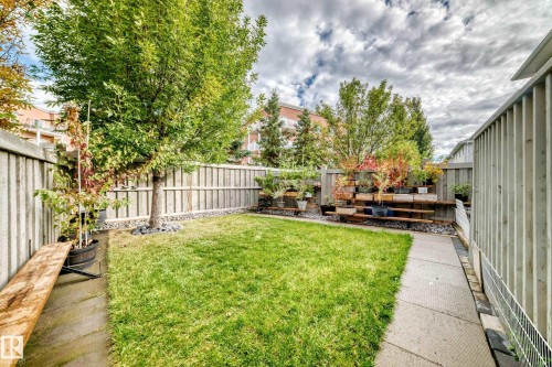 Private backyard featuring a grass lawn, paved walkways, and a wood privacy fence - #27 287 Macewan Rd Sw, Edmonton, AB 