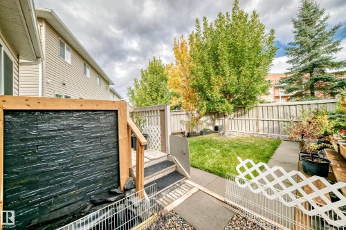 Backyard featuring a slate-tiled water feature, wood-framed deck, fenced perimeter, and a manicured lawn - #27 287 Macewan Rd Sw, Edmonton, AB 