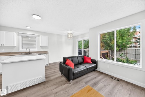Open-concept living space with wood-finish flooring, white cabinetry, integrated kitchen island, and large windows - #27 287 Macewan Rd Sw, Edmonton, AB 