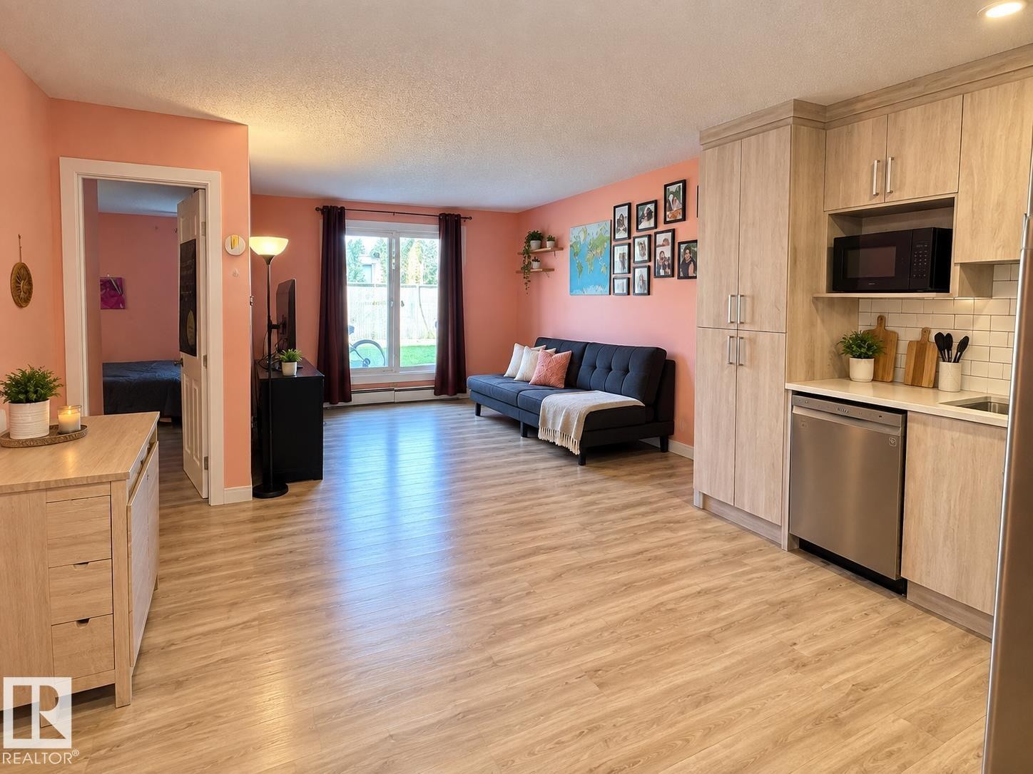 Open-concept living area with wood-finish flooring, a kitchen featuring light wood-tone cabinetry, a stainless steel dishwasher, and subway tile backsplash - #108 2624 Mill Woods Rd E Nw, Edmonton, AB