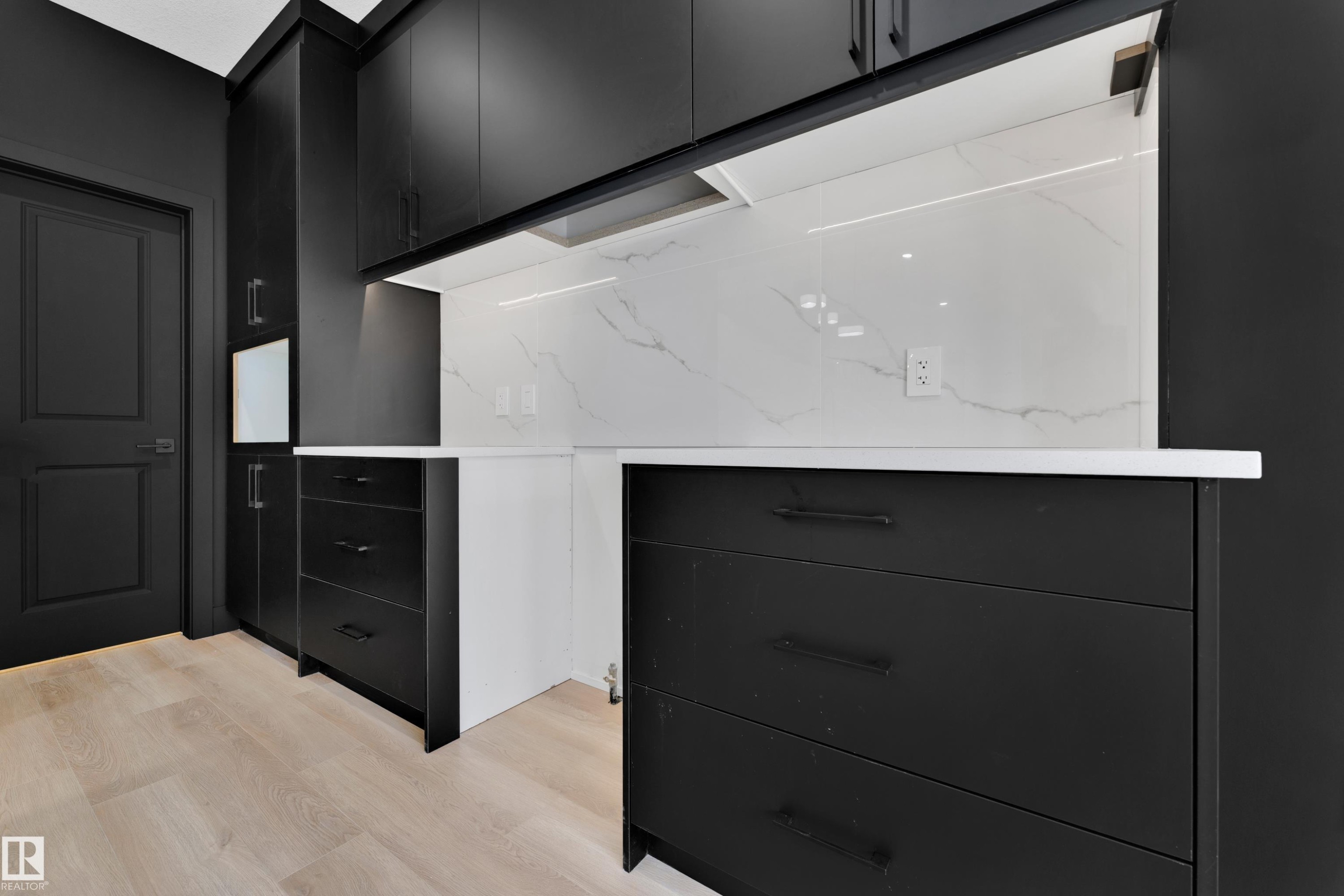 Dark cabinetry with black hardware, white countertops, white patterned backsplash, and light wood-finish flooring - 261 Linden Loop, Leduc, AB