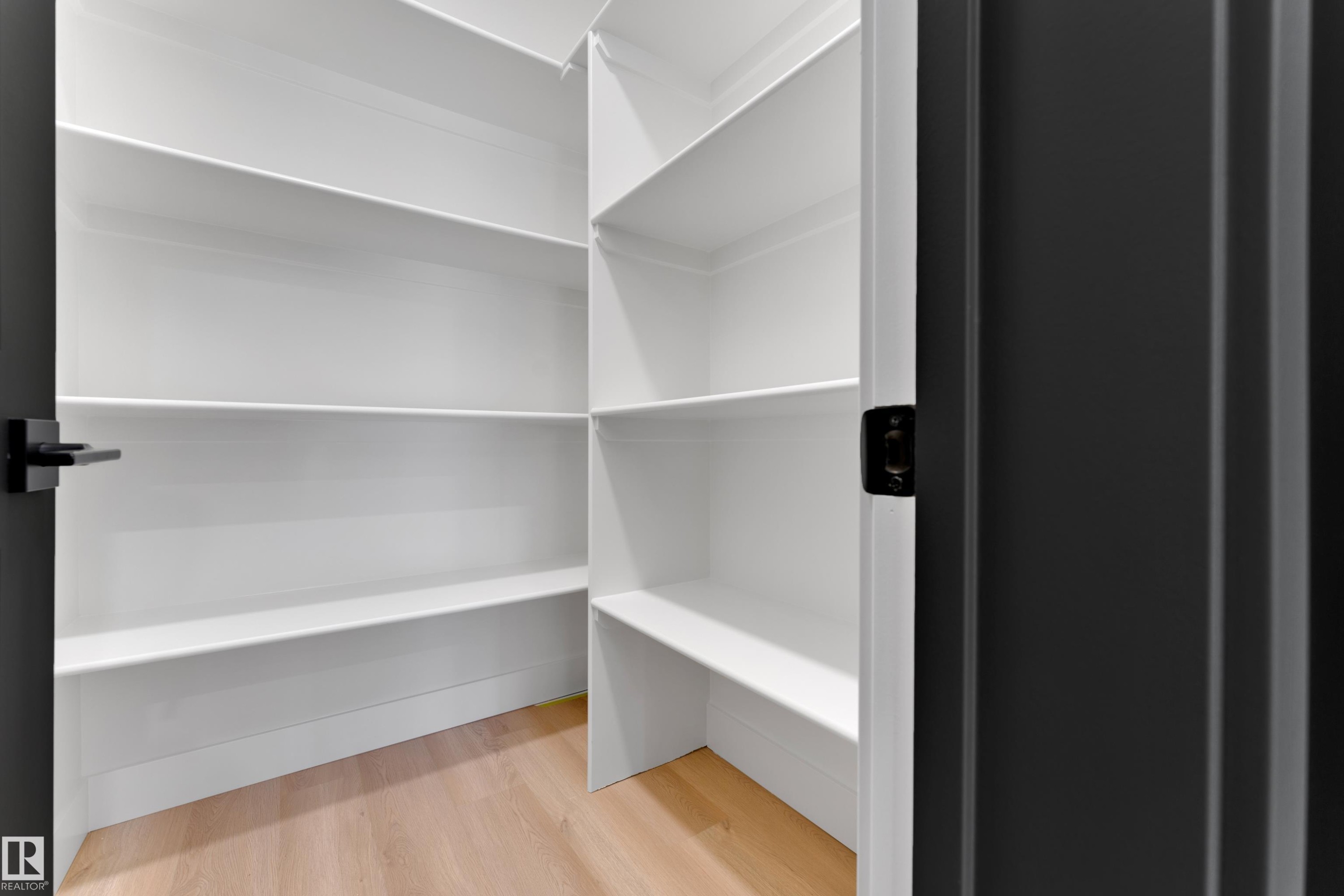 Walk-in pantry with light wood-finish flooring, white built-in shelving, and dark hardware - 261 Linden Loop, Leduc, AB