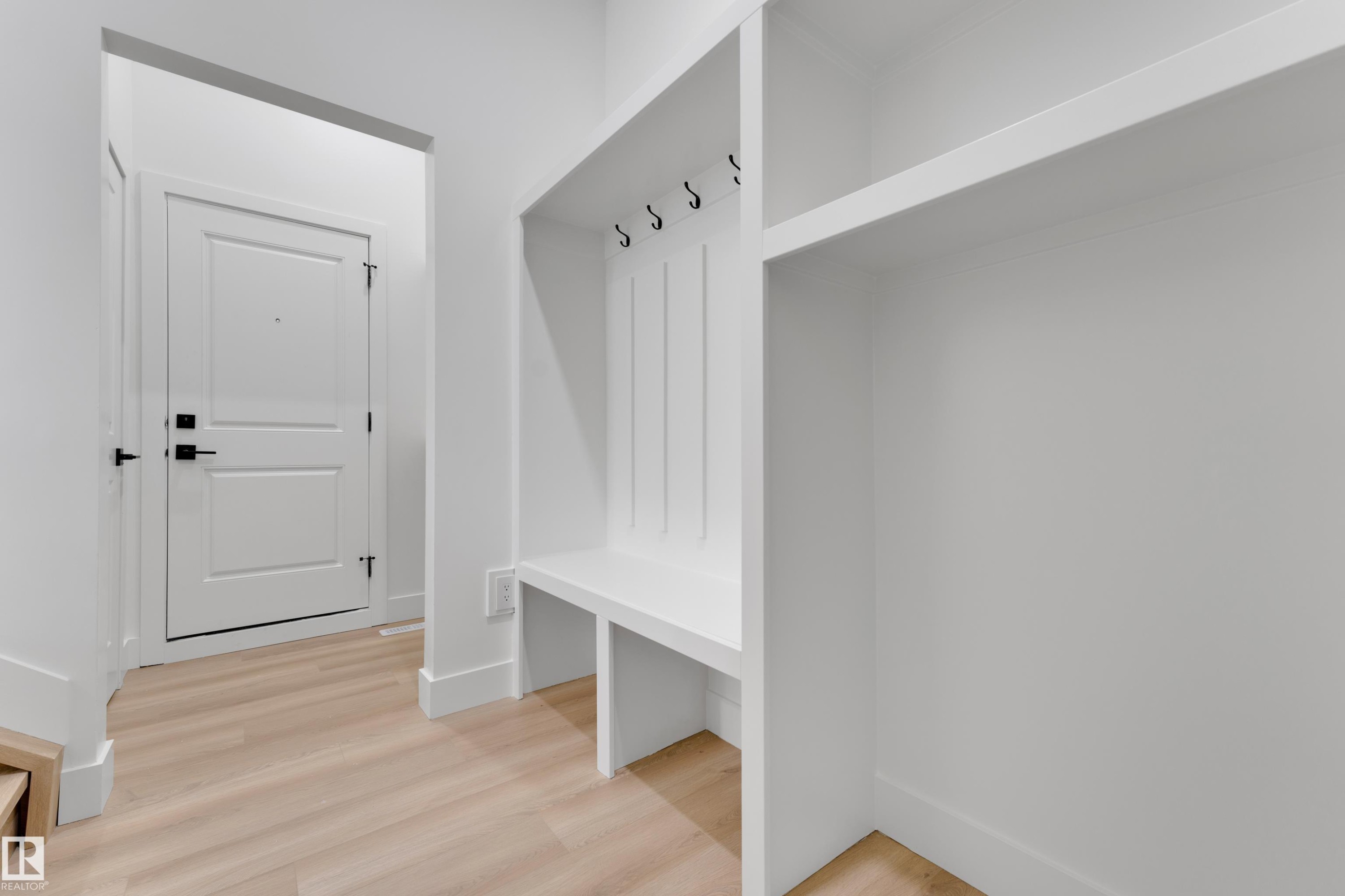 Built-in entryway bench with storage, integrated coat hooks, and overhead shelving, complemented by light wood-finish flooring - 261 Linden Loop, Leduc, AB