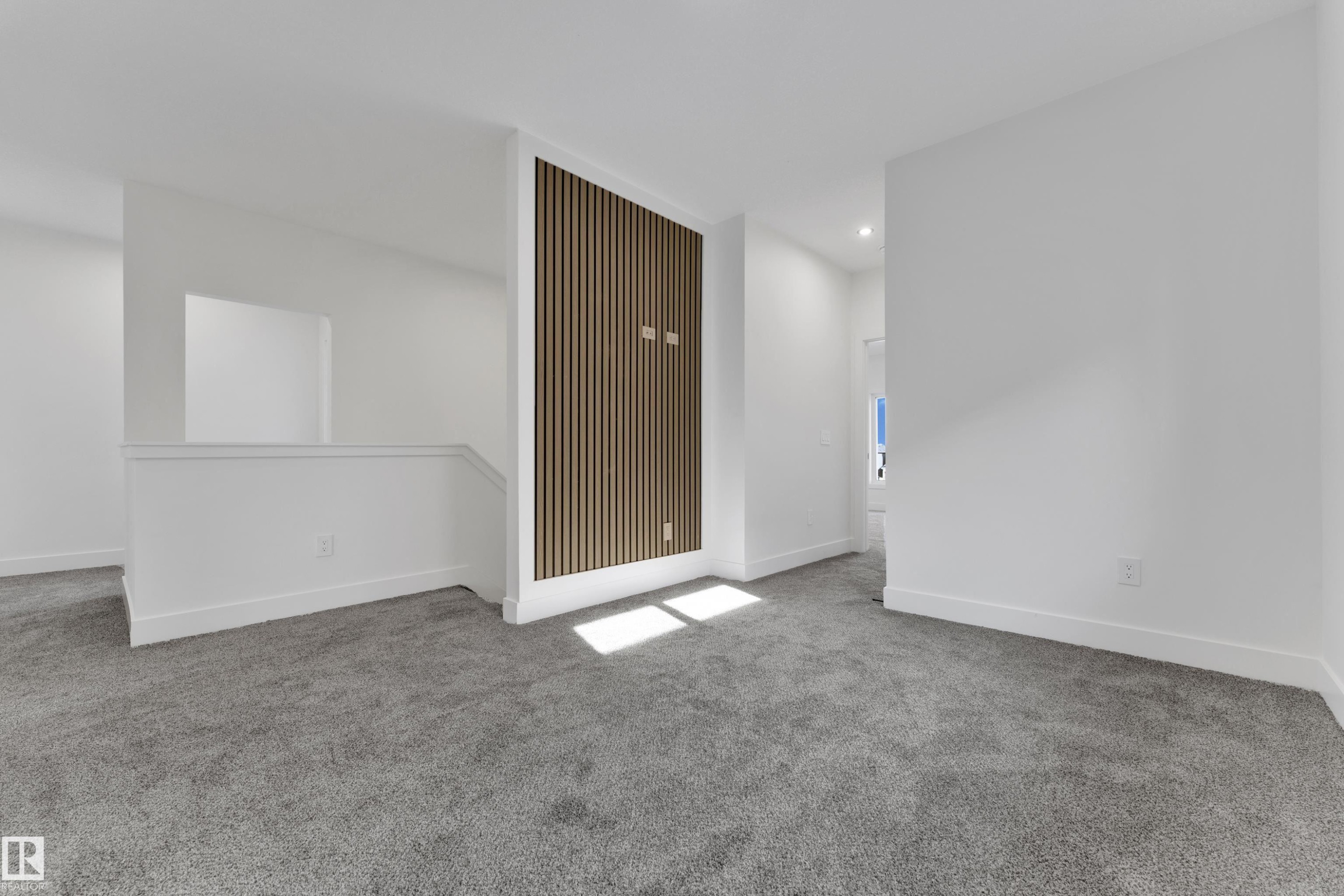 Expansive carpeted area featuring a partial wall with vertical wood paneling, white painted walls, and recessed lighting - 261 Linden Loop, Leduc, AB