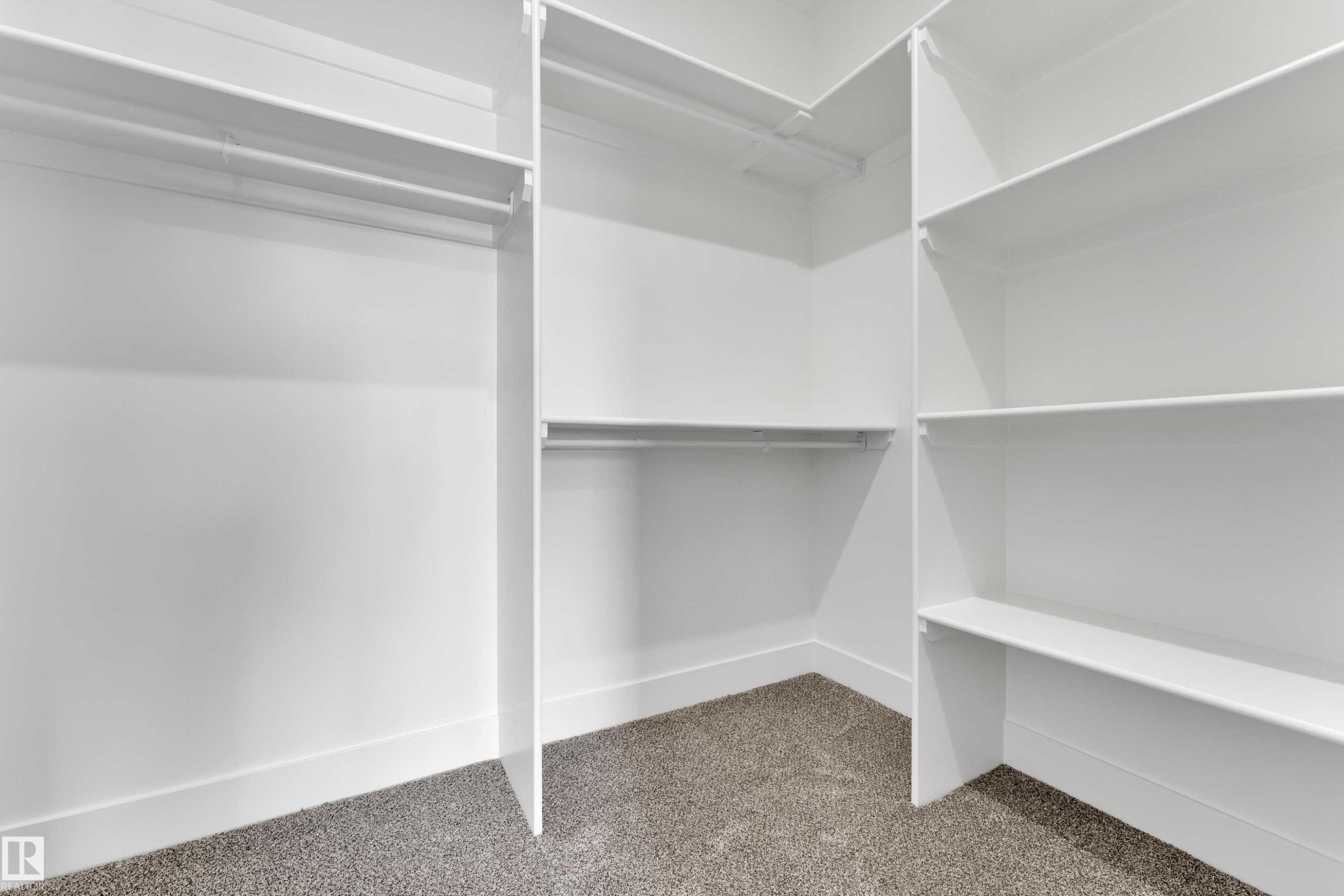 Walk-in closet featuring white built-in shelving, multiple hanging rods, and gray carpet flooring - 261 Linden Loop, Leduc, AB